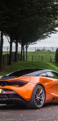 Looking for an eye-catching live wallpaper for your phone that combines stunning automotive style with picturesque natural scenery? Look no further than this incredible design featuring a bright orange sports car parked on the side of a beautiful road