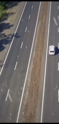 This live wallpaper features a serene view of a white car cruising down a forest-lined highway