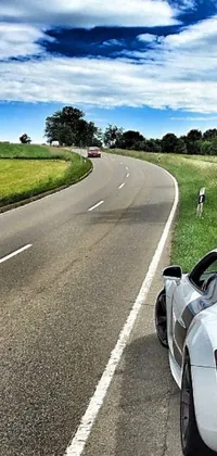This phone live wallpaper depicts a white sports car parked on a French road against a stunning backdrop