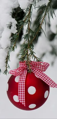This phone live wallpaper showcases a charming red ornament hanging from a snow-clad tree