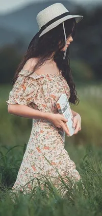 This floral phone live wallpaper showcases a woman in a summery dress and hat standing in a sun-kissed field, holding a notebook