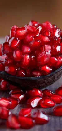 This colorful live phone wallpaper features a bowl of juicy pomegranates resting on a wooden table