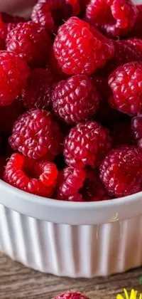 This live wallpaper features a minimalist and charming image of a white bowl filled with fresh and juicy raspberries on a wooden table