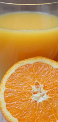 This phone live wallpaper depicts a glass of orange juice and a half of an orange, sourced from Pexels and featuring elements of Hurufiyya art