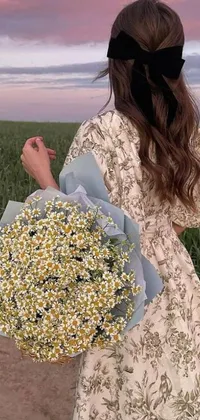 This live phone wallpaper showcases a stunning woman standing in a field while holding a bouquet of flowers wearing a beautiful floral chiton