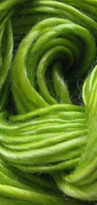 This live wallpaper is a stunning close-up shot of a pile of green yarn on a wooden table