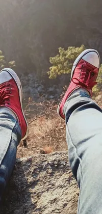 This lively phone wallpaper features a pair of striking scarlet sneakers resting atop a rocky outcropping in a scenic natural setting