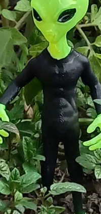 This phone live wallpaper features a close-up shot of a toy alien in a garden wearing a black 3D printed lizardfolk suit with green accents