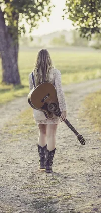 This phone live wallpaper features a blonde woman holding a guitar as she walks down a dirt road