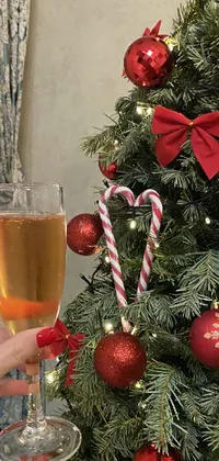 This live wallpaper for mobile depicts a young woman holding a glass of wine in front of a festive Christmas tree