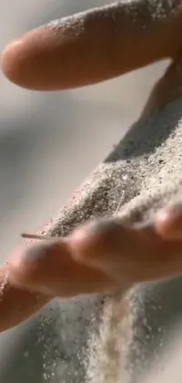 This phone live wallpaper features a close-up of a hand holding sparkling sand
