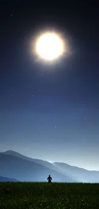 This phone live wallpaper showcases a stunning scenic image depicting a man standing on a green field beneath a bright full moon