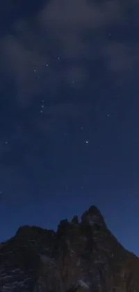 This phone live wallpaper transports you to a winter wonderland with a group of people standing atop a snow-covered mountain, set against the backdrop of a clear, starry sky