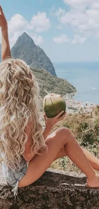 This live wallpaper features a woman with long blonde hair and a voluminous afro, sitting on a rock with a coconut in hand