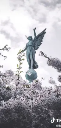 Enjoy the calming presence of an angel statue on top of a tree with this live wallpaper