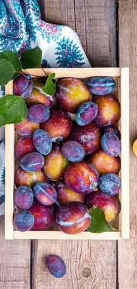 This live phone wallpaper features a vibrant box of fresh plums resting on a rustic wooden table