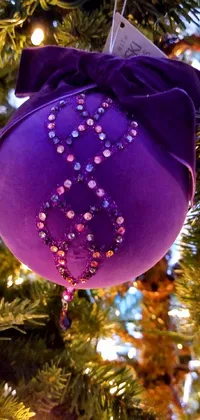 This live phone wallpaper depicts a beautifully crafted purple ornament hanging from a Christmas tree