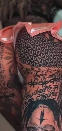 The phone live wallpaper depicts hyperrealistic tattoo designs of legs and arms, featuring gang tattoos and a stunningly detailed flower of life tattoo with intricate symbols of death and machines