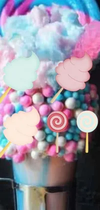 This live phone wallpaper features a cup overflowing with candy and lollipops, surrounded by cotton candy clouds and lollipop trees against a colorful cake layer background