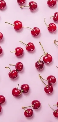 This stunning phone live wallpaper features a bunch of cherries on a pink surface, surrounded by charming emojis