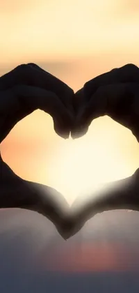 This phone live wallpaper showcases a picturesque sunrise or sunset with a person making a heart symbol