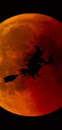 Experience the magic of this stunning phone live wallpaper featuring a witch silhouette flying on a broom in front of a striking red and orange blood moon