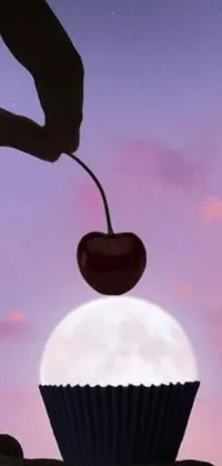 This live wallpaper for your phone is truly unique with its surreal image of a cherry being held over a delicious cupcake