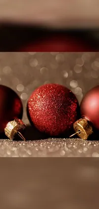Enhance your phone's look with a stunning live wallpaper of a showpiece featuring three Christmas balls in a brilliant maroon red hue, exquisitely reflected by glitter that adds a touch of festive vibrancy