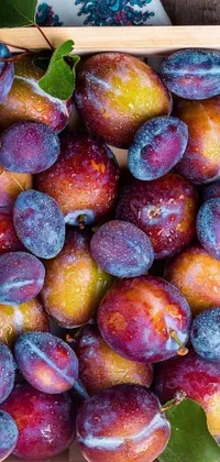 This phone live wallpaper features a wooden table as a backdrop with a box of ripe, juicy plums resting on top
