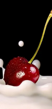 This phone live wallpaper features a stunning digital art image of a red cherry falling into a glass of white milk