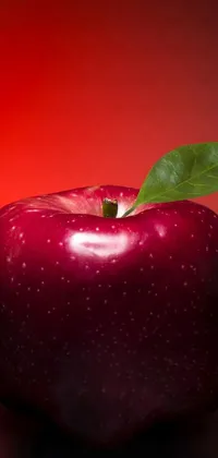 Introduce a vivid live phone wallpaper of a shiny red apple with a green leaf resting on top