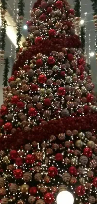 This phone live wallpaper features a large Christmas tree adorned with red and white ornaments against a mall background