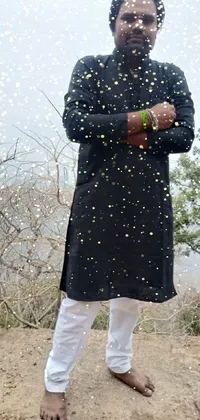 This unique phone live wallpaper depicts a man standing on a dirt hill, wearing stylish black modern clothing while gazing out into the distance