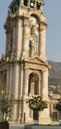 This live phone wallpaper displays a stunning clock tower with neoclassical architecture and intricate designs, accompanied by a beautifully crafted statue and the picturesque backdrop of the mountains and old city of Guanajuato