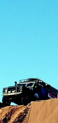 This stunning live phone wallpaper showcases a rugged truck driving on a sandy hill in the desert against a beautiful blue sky backdrop