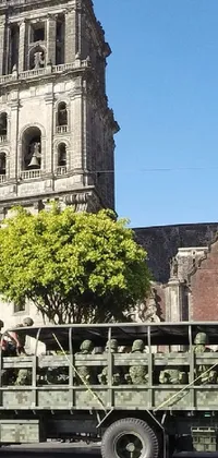 This dynamic mobile wallpaper captures a group of military trucks driving down a city street in Mexico, with an ancient cathedral serving as a stunning backdrop