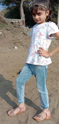 This phone live wallpaper showcases a little girl wearing stylish jeans and a t-shirt while standing on a beautiful sandy beach