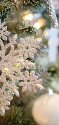This charming phone live wallpaper showcases an enchanting snowy scene with beautiful snowflakes and gleaming silver ornaments hanging from a lush green Christmas tree