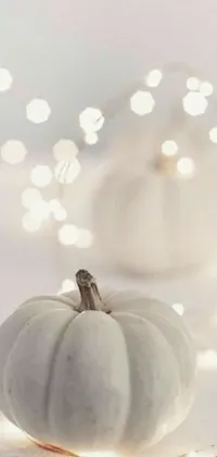Looking for a mesmerizing live wallpaper for your phone? Look no further than this stunning design featuring a beautifully carved white pumpkin resting on a wooden table