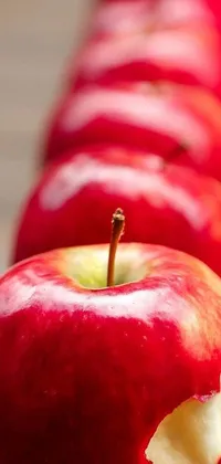 Decorate your phone with a beautiful live wallpaper showcasing a row of red apples sitting on a wooden table