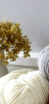This cozy live wallpaper showcases two fluffy balls of yarn sitting on a rustic wooden table surrounded by knitting materials, brushes and foliage in the autumn season