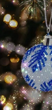 Experience the holiday spirit with this stunning phone live wallpaper featuring a cross-stitched blue and white ornament hanging from a Christmas tree adorned with luminous sparkling crystals