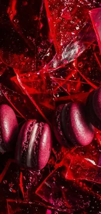 This phone live wallpaper displays a close-up view of colourful macarons atop a pile of broken glass, featuring a red atmosphere and dark purple colour scheme