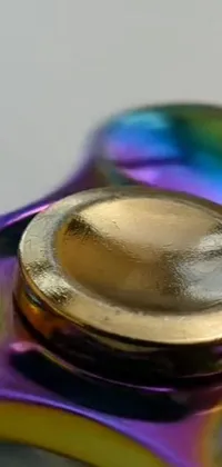 This colorful live wallpaper for phones features a macro photograph of a brass wheel fidget spinner sitting on a wooden table
