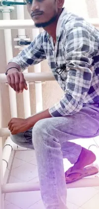 This phone live wallpaper depicts a serene scene featuring a man sitting on a white chair, wearing a plaid shirt and jeans