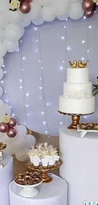 This beautiful phone live wallpaper depicts a table adorned with a cake and cupcakes in a white and gold color scheme
