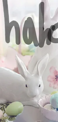 Get into the Easter spirit with this adorable live wallpaper featuring a fluffy white bunny sitting on a table surrounded by colorful eggs