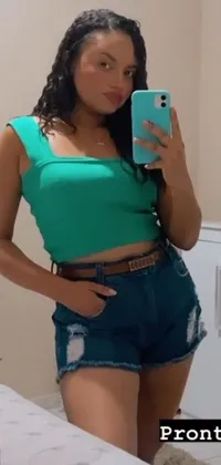This phone live wallpaper features a woman taking a selfie in front of a mirror wearing a green halter top and short jeans