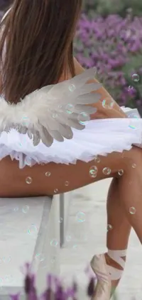 Experience a magical and ethereal vibe with this phone live wallpaper featuring a woman with angel wings sitting on a bench
