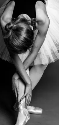 This captivating live wallpaper displays a monochrome photograph of a ballet dancer tying up her ballet shoes